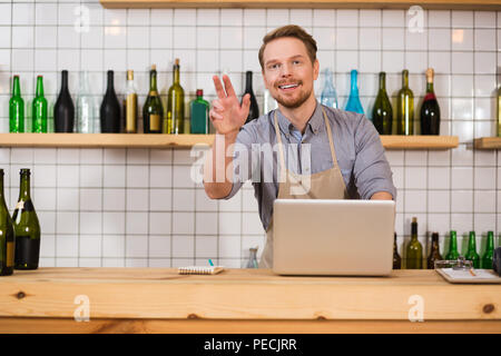 Caffetteria lavoratore. Positivo bello uomo barbuto che indossa il grembiule e permanente al contatore mentre si lavora nella caffetteria Foto Stock