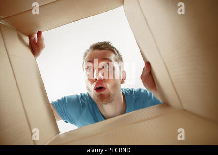 Uomo sorridente, apertura della casella e guardando all'interno. Il pacchetto, consegna, sorpresa, dono e il concetto di stile di vita Foto Stock