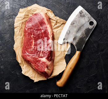 Crudo fresco di carne in marmo nero bistecca angus e carni cleaver su carta marrone. Carne su sfondo nero con copia spazio. Vista dall'alto. Foto Stock