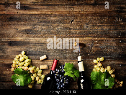 Le bottiglie di vino con uve su legno sfondo rustico con copia spazio. Vino rosso e bianco. Vista dall'alto. Foto Stock