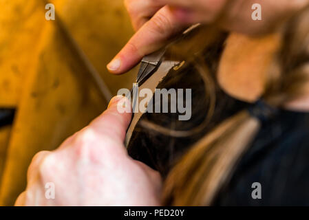 Lavorando con pinza su un pezzo di gioielleria in officina con l' aiuto di adattamento delle attrezzature e orafo e permanente tenendo con entrambe le mani Foto Stock