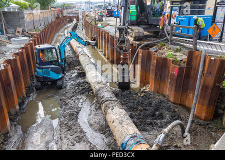 Mini escavatore lavorando su una trincea di scavo accanto a una pipeline accanto alla cassaforma metallica. Foto Stock