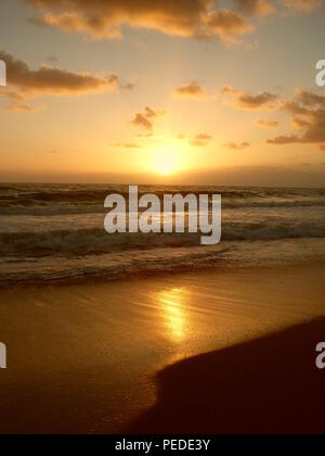 Romantischer Sonnenuntergang am Meer, der alles in goldenes Licht taucht und zum Träumen verführt Foto Stock