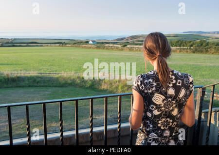 Una giovane donna in piedi su un balcone che guarda al mare. Foto Stock