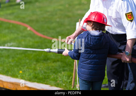 Firefighter aiutare un giovane ragazzo con un modello Firehose durante una dimostrazione Foto Stock