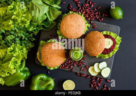 Hamburger vegano con fettine di barbabietole e frullati verdi su sfondo nero. Sano cibo vegan. Detox dieta. Lay piatto. Foto Stock