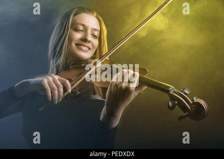 La donna a suonare il violino contro uno sfondo scuro. La nebbia in background. Studio shot Foto Stock