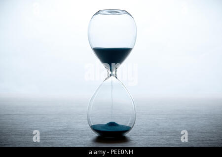 Clessidra con sabbia blu su uno sfondo bianco e grigio di una tabella da vicino Foto Stock