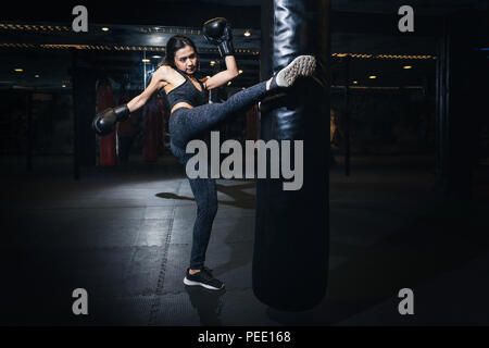 Boxer femmina di colpire un enorme sacco da boxe presso un studio di inscatolamento. Donna boxer allenamento duro. Thai boxer punch kick da sacco da boxe, bacground nero Foto Stock