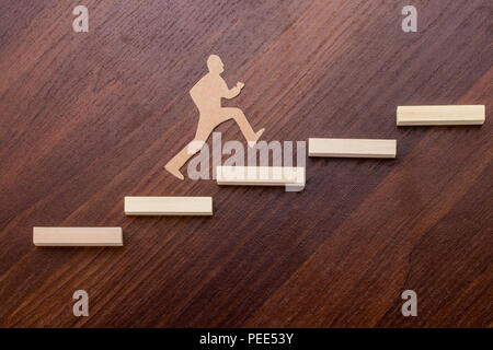 Ritagli di carta uomo salire gli scalini per raggiungere il successo in una immagine concettuale su sfondo di legno. Foto Stock