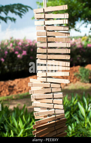 Lavanderia in legno clip abbigliamento appeso verticalmente su una stringa in country house cortile sulla vegetazione verde sullo sfondo Foto Stock
