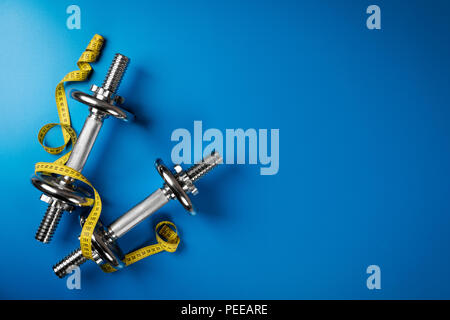 Manubri e nastro di misurazione su sfondo blu con spazio di copia Foto Stock