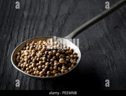 Raw, organici grezzi o di coriandolo Semi di coriandolo in metallo sul cucchiaio di legno scuro tabella Foto Stock