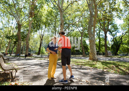 Vestiti in maniera colorata gli uomini italiani sia con cappelli di paglia per incontrare e salutare ogni altro su una mattina estati al parco. Piacenza, Italia. Foto Stock