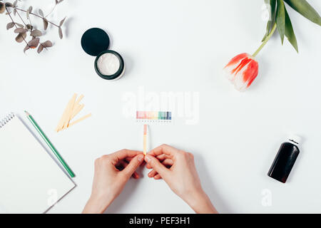 Donna sperimentazione dei cosmetici il livello del pH utilizzando la cartina di tornasole e scala di colori. Vista superiore della mano femminile di reazione corrispondenti a colori su sfondo bianco. Foto Stock