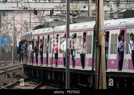 Passeggeri appendere fuori della porta di treni su Mumbai la ferrovia suburbana in treno arrivando alla stazione di Bandra di Mumbai, India Foto Stock