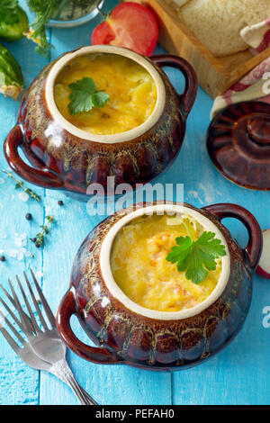 Patate e pesce rosso con crema di formaggio e cuocere in pentole di creta in cucina lo sfondo di legno. Cucina russa. Foto Stock