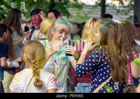 DZERZHINSK, RUSSIA - 19 MAGGIO 2018: La giovane ragazza felice sta controllando il suo make-up facciale usando smartphone sul festival dei colori e della musica di Holi. Foto Stock