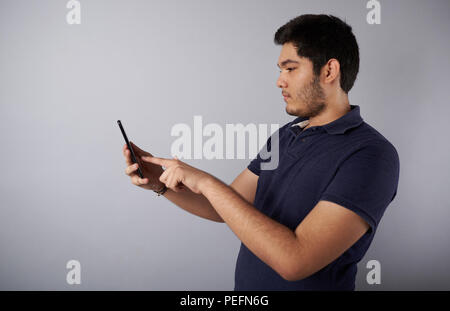 Giovane uomo utilizza lo smartphone vista di profilo su grigio di sfondo per studio Foto Stock