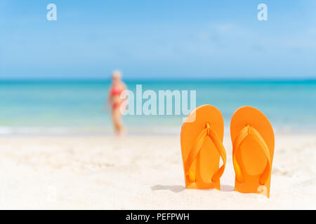 Felice bella giovane donna in bikini rosa con flip flop sulla spiaggia sabbiosa, verde mare e cielo azzurro sfondo per le vacanze estive e il concetto di vacanza. Foto Stock