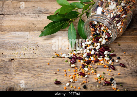 Una dieta salutare concetto. Assortimento di legumi in un vasetto di vetro e versato su di un tavolo di legno sfondo, copia dello spazio. Foto Stock