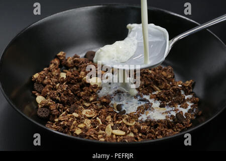 Il latte fluisce sul cucchiaio in cioccolato muesli, cereali Foto Stock