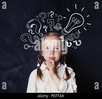 Smart bambino schoolgirl con lampadina e chalk interrogativi sulla scuola di blackboard sfondo. Idea concept Foto Stock