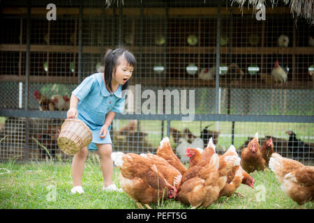 Felice bambina polli di alimentazione nella parte anteriore della fattoria di pollo. Attività estive per bambini. Foto Stock