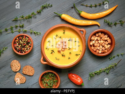 Zuppa di zucca in vaso in ceramica su grigio legno rustico servita con timo e crostini. Accanto ad essa sono il peperoncino, foglie di timo e crostini. Piatto, laici vi Foto Stock