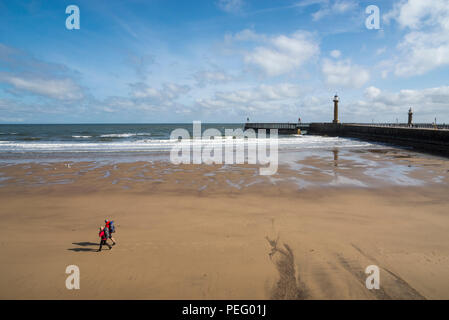 Paio di camminare sulla spiaggia a Whitby sands sulla costa del North Yorkshire, Inghilterra. Foto Stock