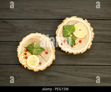 Taglio del legno con con fettine di limone e melograno bacche su sfondo nero Foto Stock