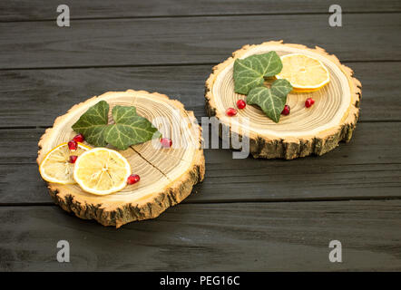 Taglio del legno con con fettine di limone e melograno bacche su sfondo nero Foto Stock