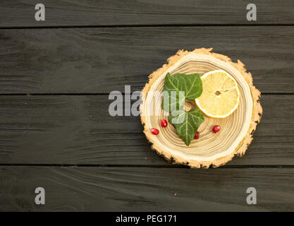 Taglio del legno con con fettine di limone e melograno bacche su sfondo nero Foto Stock