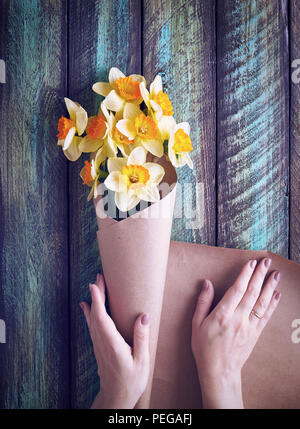 Donna di incarto bouquet di narciso in carta marrone sul verde sullo sfondo di legno Foto Stock