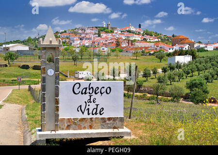 Segnale di ingresso in forma di una chiesa e di visualizzare al villaggio idilliaco Cabeco de Vide su una morbida collina verde circondato da alberi di olivo Foto Stock