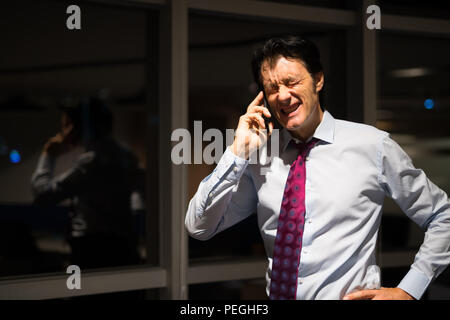 Sottolineato imprenditore maturo in Office di notte parlando al telefono cellulare Foto Stock