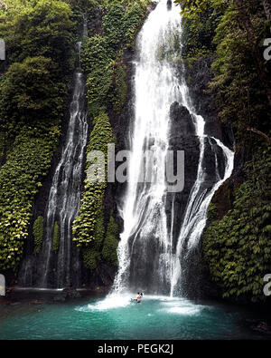 Cascata cascata nella foresta pluviale tropicale con coppia in amore la balneazione al di sotto. Luna di Miele romantica vacanza in banyumala twin cascata Foto Stock