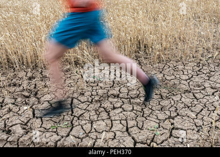 Uomo che corre su terra rotto durante la siccità. Regno Unito. Il cambiamento climatico e il riscaldamento globale del concetto. Foto Stock