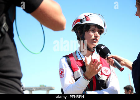 Genova, Italia. Il 15 agosto, 2018. Federica Bornelli, della Croce Rossa Italiana, risponde alle domande dei giornalisti. Un giorno dopo il crollo del ponte dell'autostrada Ponte Morandi (fondo), è ancora in fase di ricerca per i superstiti in enormi macerie. Credito: Fabian Nitschmann/dpa/Alamy Live News Foto Stock