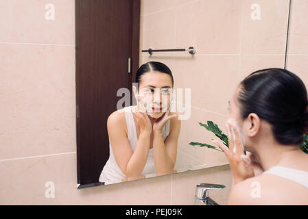 Donna felice deterge la pelle con la schiuma in bagno. Foto Stock