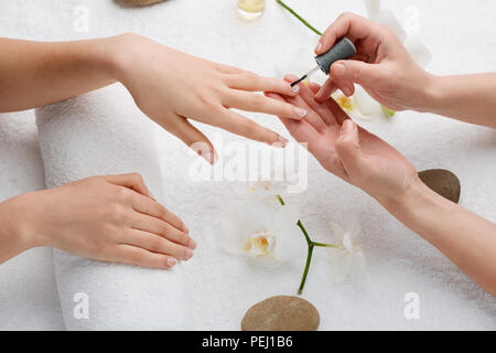 Il tecnico l'applicazione di patina di base sulle unghie. Atmosfera accogliente e il divertimento di coccole. Perfetto french manicure al salone. Foto Stock