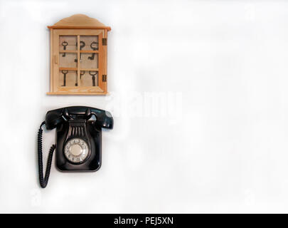 Vecchio nero telefono e archiviazione in legno con chiavi differenti sul muro bianco Foto Stock