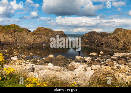 Vista panoramica di Ballintoy, Co Antrim, Irlanda del Nord in estate con due persone in un momento di relax a bordo dell'acqua Foto Stock