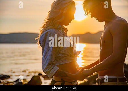 Silhouette di coppia in amore abbracciando in spiaggia contro il sole Foto Stock