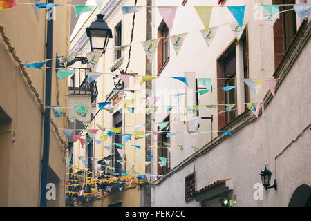 Strada stretta con giallo facciate di case, lanterna e bandiere decorativi nel quartiere storico di Tossa de Mar, Spagna Foto Stock