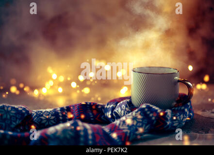 Atmosfera accogliente con inverno caffè o tè mug con vapore coperto con lana sciarpa su luci bokeh di fondo Foto Stock