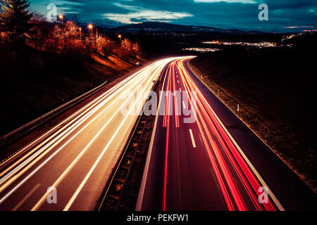 Una lunga esposizione night shot di una autostrada da regione di Friburgo in Svizzera con rosso luce del veicolo sentieri e luci di pubblico Foto Stock