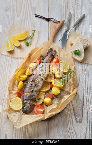 Limone al forno trota al forno con rosmarino arrosto patate e pomodori, servita sulla carta da forno Foto Stock