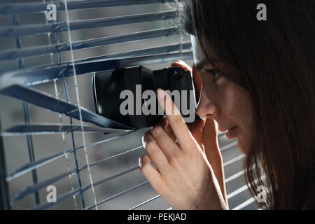 Giovane donna Paparazzi per scattare una foto con sospetto dal intorno a persiane mentre si utilizza una telecamera. Il PILR Concept Foto Stock