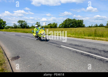 Motociclista della polizia che corre a velocità sostenuta mentre ferma il traffico durante la gara ciclistica OVO Energy Tour of Britain. Strada. Campagna Foto Stock